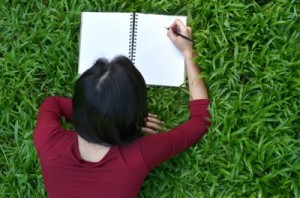 Woman author with maroon shirt with pencil writing a non-fiction book.